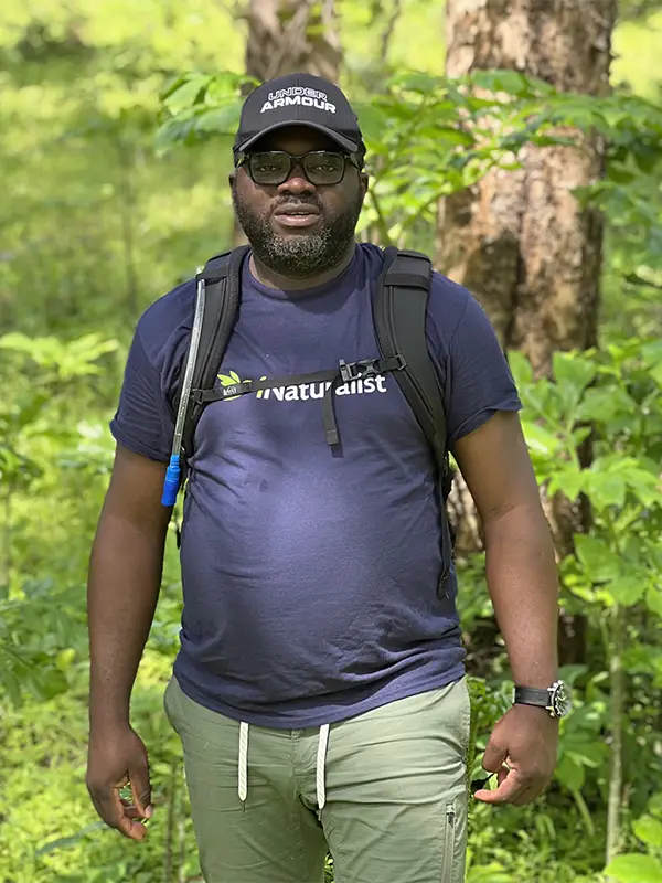 Photo of Orou Gaoue in the woods wearing a hat and backpack