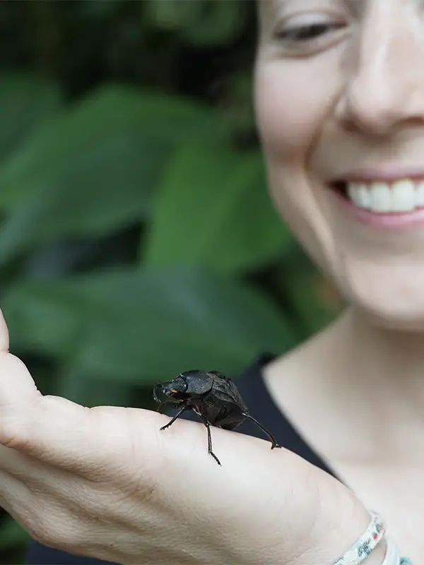 An insect crawling on a woman's hand with greenery in the background